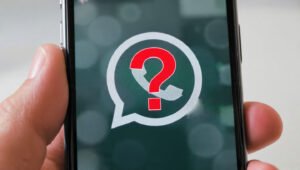 A hand holds a smartphone displaying a blurry WhatsApp logo with a red question mark in the center